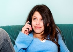 Girl with blue jumper and brown hair, sitting on a green sofa with the telephone to her right ear.