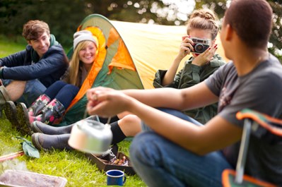 Group of young people camping a field with a tent in the background.