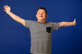 Boy with additional needs smiling with arms wide open with happiness.