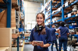 Young person wearing ear-defenders and smiling on work experience in a warehouse. 