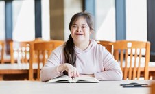 Young person with learning difficulties reading a book and smiling.