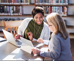 Two adults in a work environment having a discussion with laptop and notes.