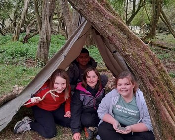 A group of young people smiling inside a bivouac shelter in the woods.