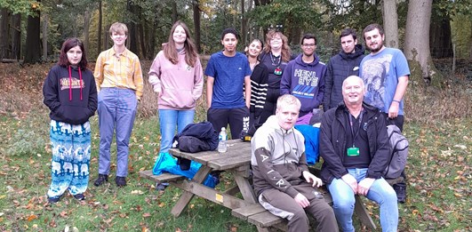 A group of Young Commissioners standing behind a picnic bench in the woods at Hudnall Park.