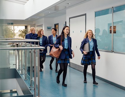 Group of young people wearing school uniform walking down a school corridor.