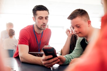 Youth worker supporting a young person with learning disabilities on a mobile phone.