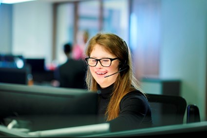 Young person with a disability talking on a headset in front of a computer in an office.