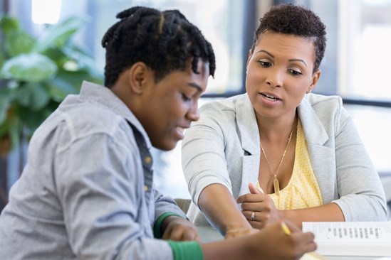 Young person writing and talking to a youth worker.