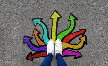 Young person's feet standing on a pavement painted with multicoloured arrows.