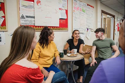 Group of young people sat around a table talking.