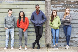 Group of young people outside standing against some weathered garage doors.