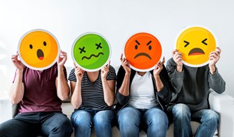 Group of people sat down holding signs in front of their faces depicting different emojis.