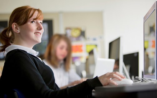 Young person sitting in front of a computer at school smiling.