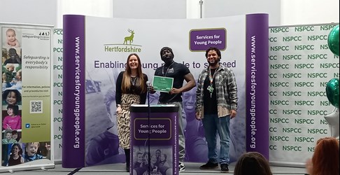 Three people standing at a podium smiling having received a certificate