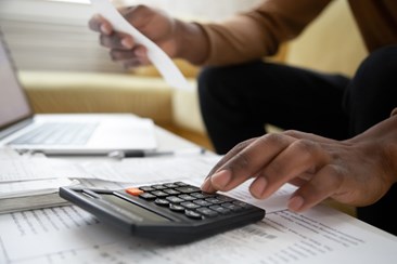 Young person's hands using a calculator to add up expenditure from receipts.