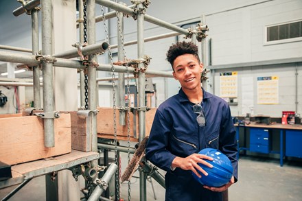 Apprentice in a workshop holding a hard hat.