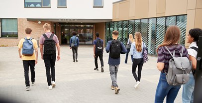 Young people walking into college in a group wearing backpacks.