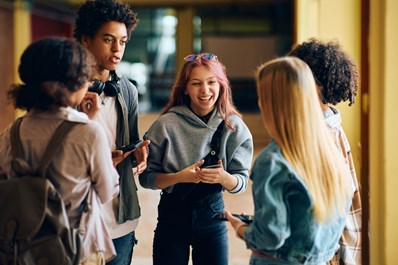 Group of young people standing in a corridor talking and holding their mobile phones.