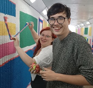 A young woman and a young man working on a mural in an underpass