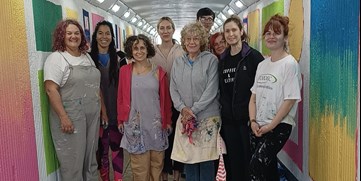 A group of nine people smiling in a brightly painted underpass