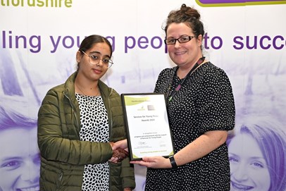 A young woman shaking hands with an older woman who is presenting her with a certificate